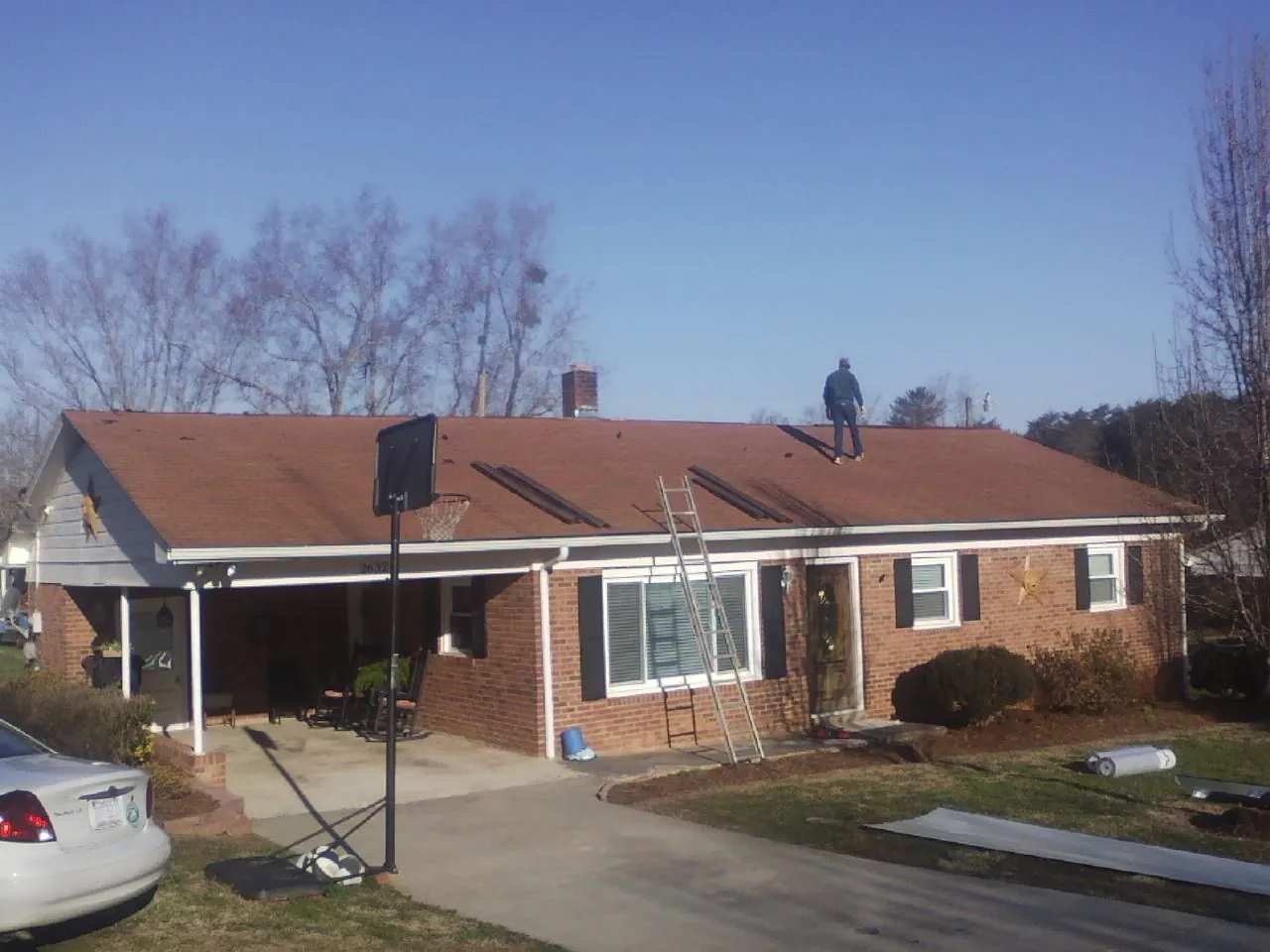 Roofer stripping a shingle roof on a brick ranch before metal panels in Strasburg