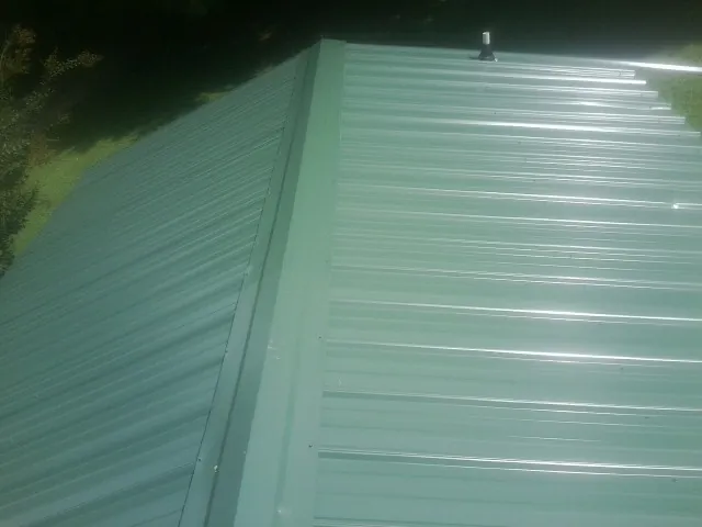 New green metal panels meeting at the ridge of a roof — Flat Roof Repair work by our crew in Strasburg